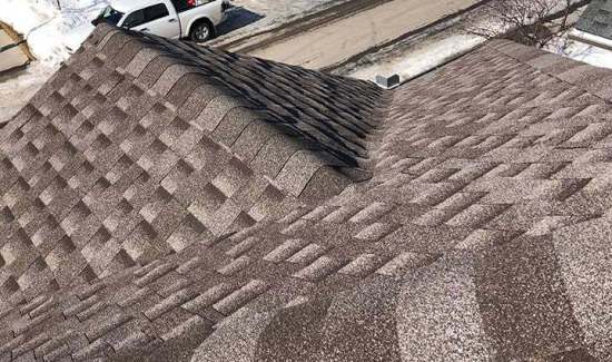High-angle view of dark architectural asphalt shingles, hip ridge capping, and a square roof vent cap installed by AKRoN Roofing.