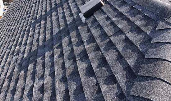 Close-up textured view of dark dimensional asphalt architectural shingles, ridge cap shingles, and a roof vent cap installed by AKRoN Roofing.