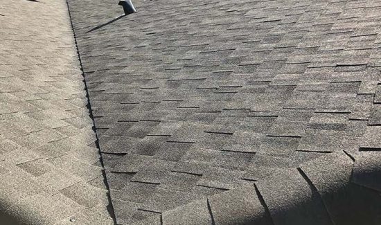 Close-up view of grey dimensional asphalt shingles, roof valley flashing, and hip ridge capping inspected by AKRoN Roofing.