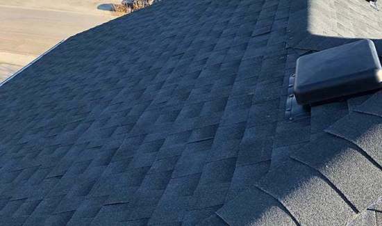 High-angle view of dark architectural asphalt shingles, hip ridge capping, and a square roof vent cap installed by AKRoN Roofing.