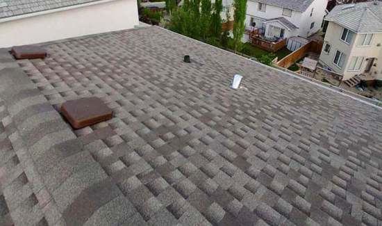 Elevated view of a multi-tone grey architectural shingle roof with roof ventilation caps, ridge capping, and pipe flashing installed by AKRoN Roofing.