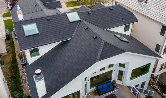 High-angle aerial view of a multi-gabled white modern house featuring a dark architectural shingle roof, skylights, and roof vents installed by AKRoN Roofing.