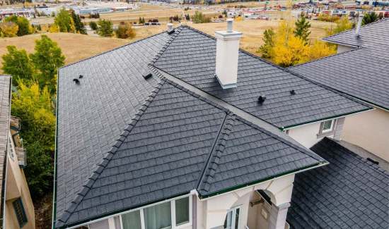 High-angle aerial view of a luxury suburban house featuring a dark composite slate tile roof, white chimney, and ridge capping installed by AKRoN Roofing.