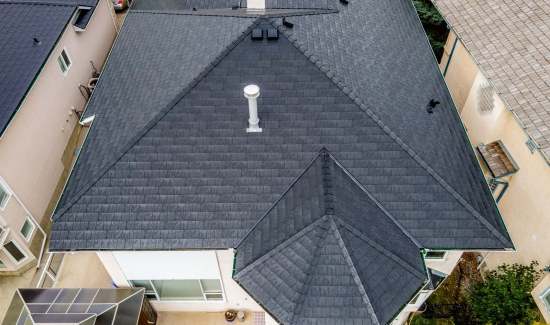 Top-down aerial drone view of a dark composite slate tile roof with multi-hipped ridge lines and chimney flashing installed by AKRoN Roofing.