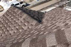 High-angle view of dark architectural asphalt shingles, hip ridge capping, and a square roof vent cap installed by AKRoN Roofing.