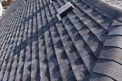 Close-up textured view of dark dimensional asphalt architectural shingles, ridge cap shingles, and a roof vent cap installed by AKRoN Roofing.