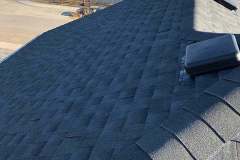High-angle view of dark architectural asphalt shingles, hip ridge capping, and a square roof vent cap installed by AKRoN Roofing.