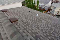 Elevated view of a multi-tone grey architectural shingle roof with roof ventilation caps, ridge capping, and pipe flashing installed by AKRoN Roofing.