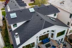 High-angle aerial view of a multi-gabled white modern house featuring a dark architectural shingle roof, skylights, and roof vents installed by AKRoN Roofing.