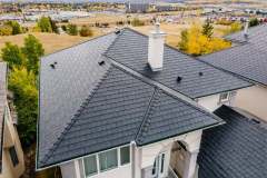 High-angle aerial view of a luxury suburban house featuring a dark composite slate tile roof, white chimney, and ridge capping installed by AKRoN Roofing.