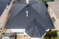 Top-down aerial drone view of a dark composite slate tile roof with multi-hipped ridge lines and chimney flashing installed by AKRoN Roofing.